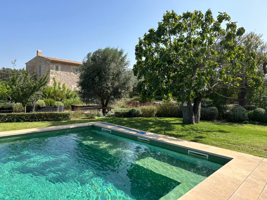A stone Mallorcan house seen across its garden and pool
